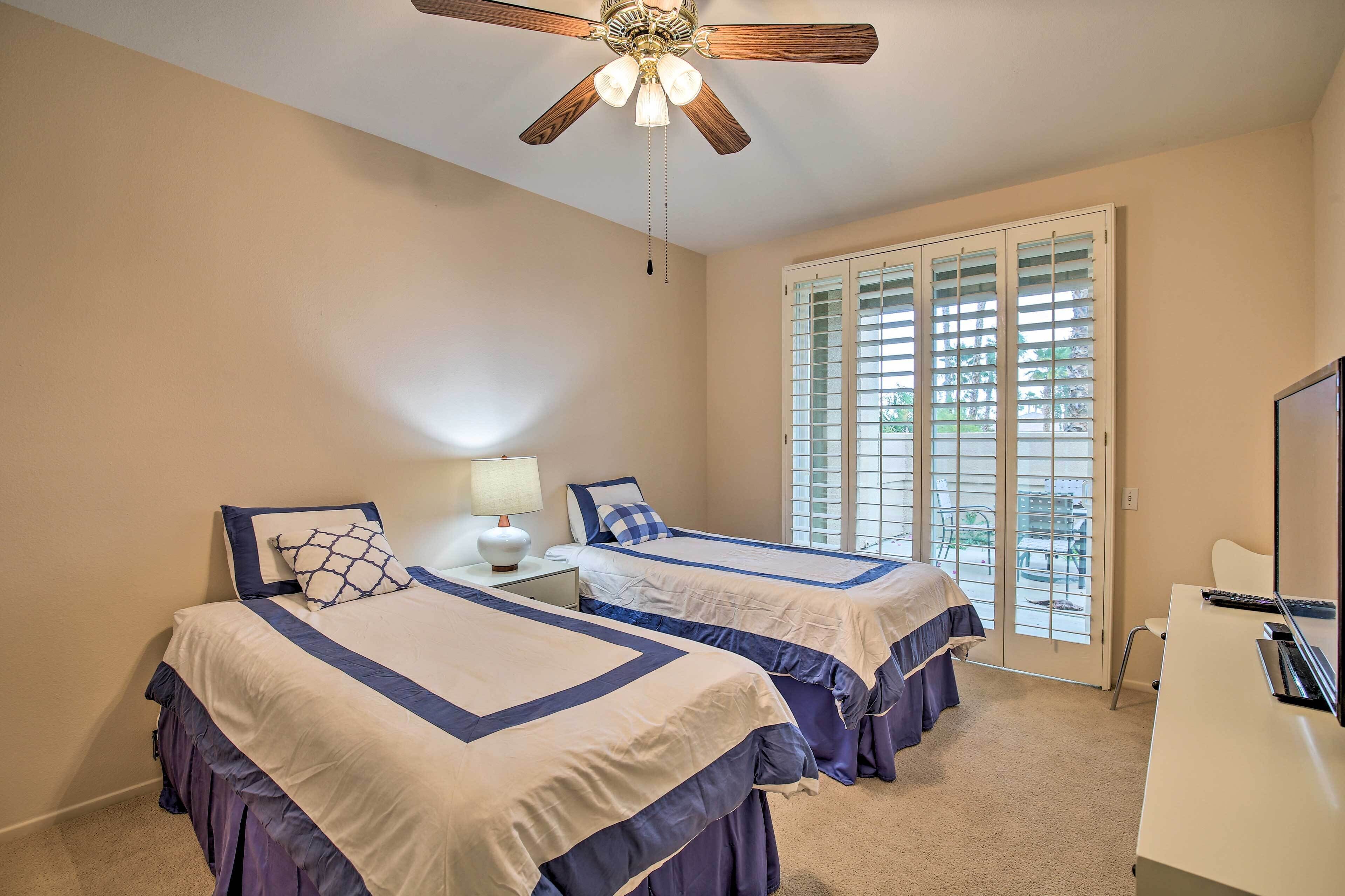 A bedroom with two beds, a ceiling fan, a desk, and a window with blinds.