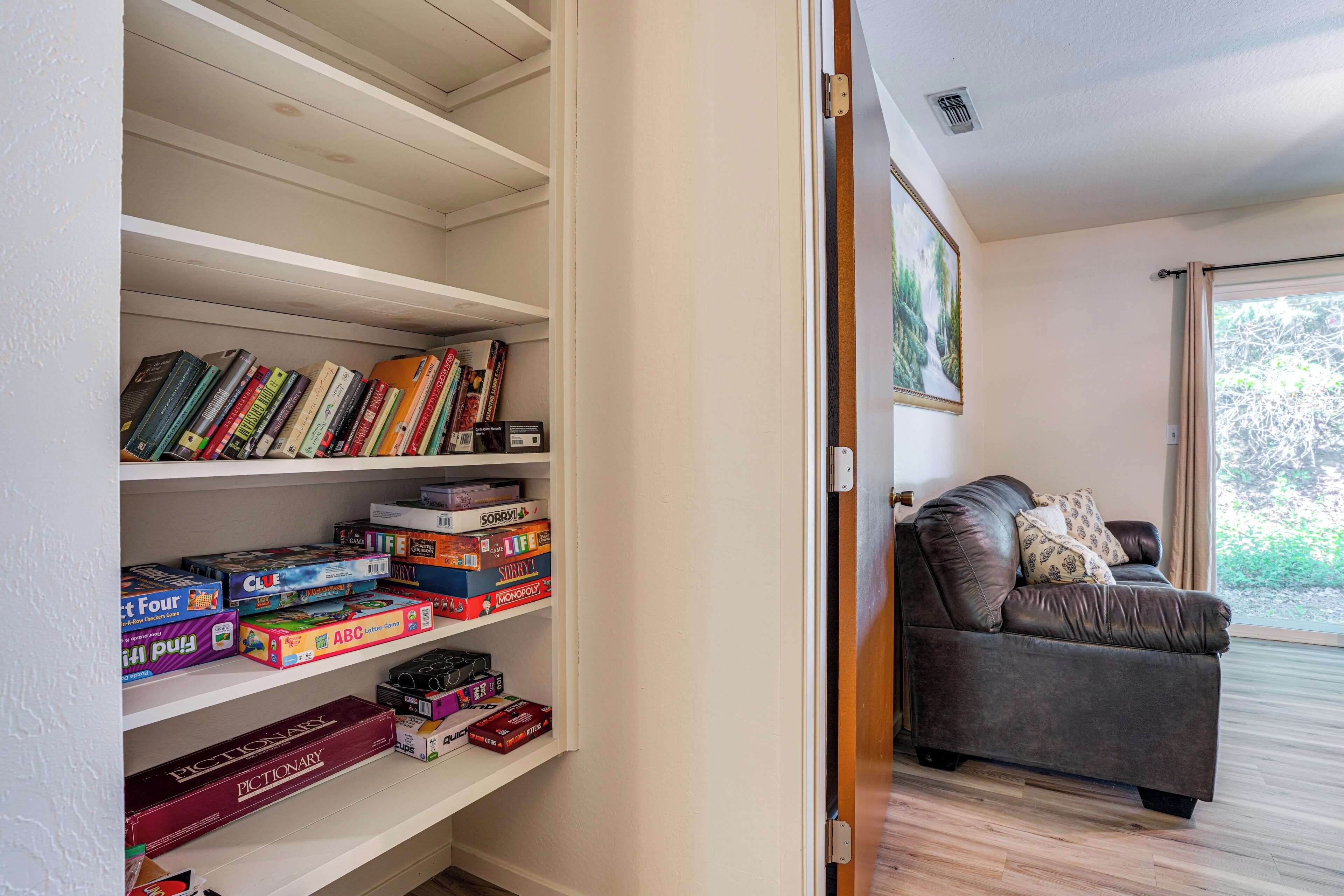 A room with a bookshelf filled with board games, a leather sofa, and a large window.