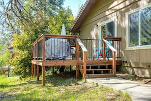 Eine Holzterrasse mit überdachter Sitzgruppe, eine Treppe, die zu einer Veranda führt, und ein Haus mit Fenstern und einer Tür.