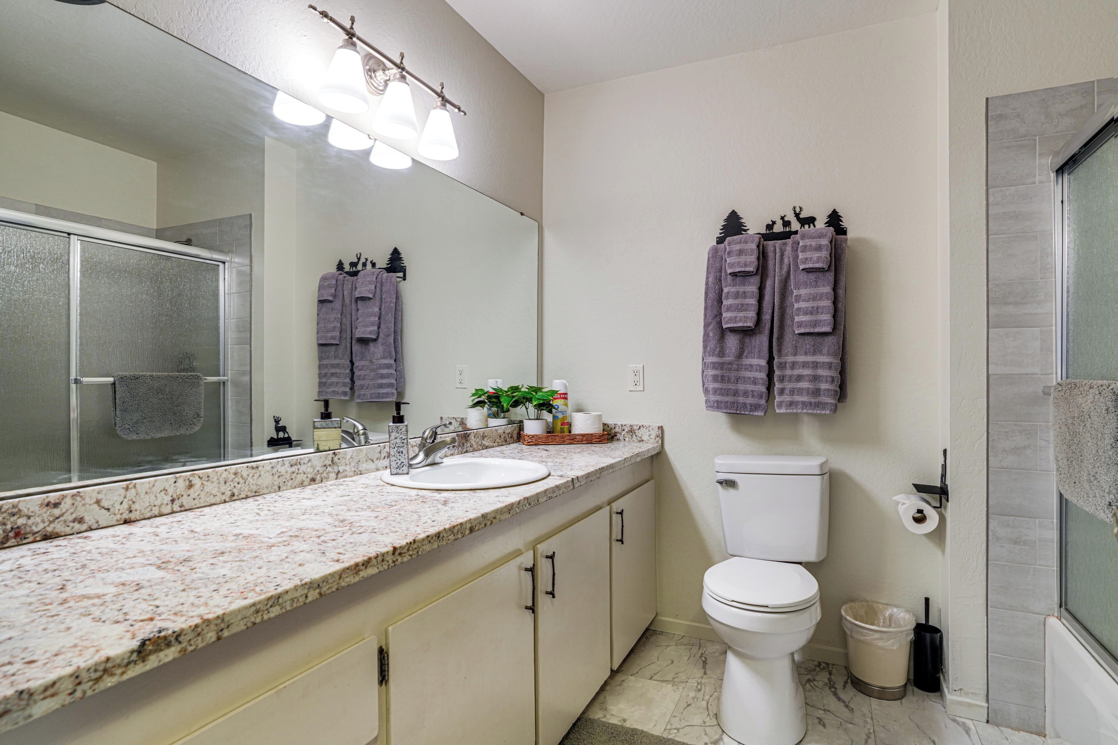 Un baño con encimera de granito, un lavamanos blanco, inodoro y zona de ducha.