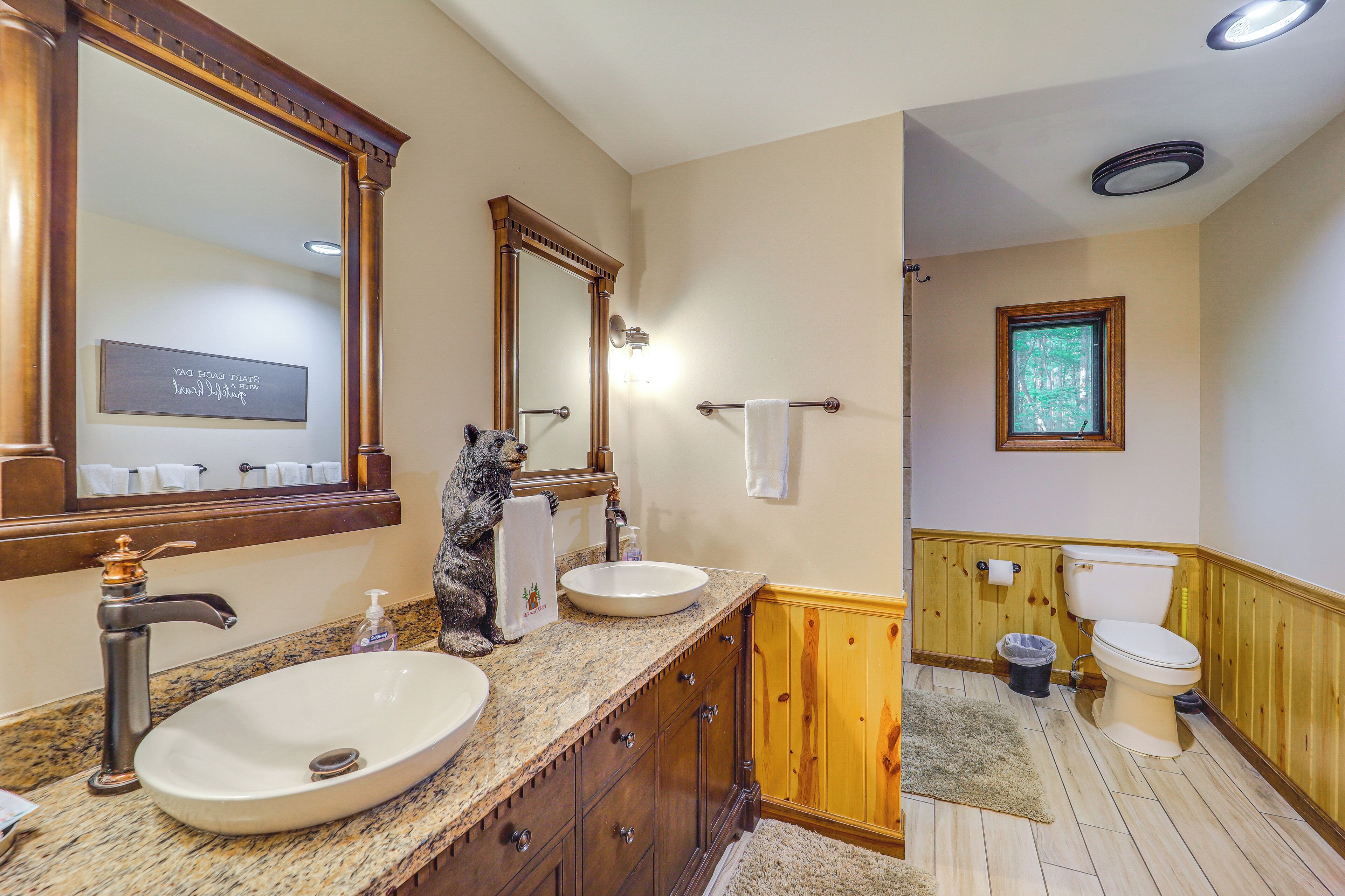 Een badkamer met een grote spiegel, een wastafel, een toilet en een raam.