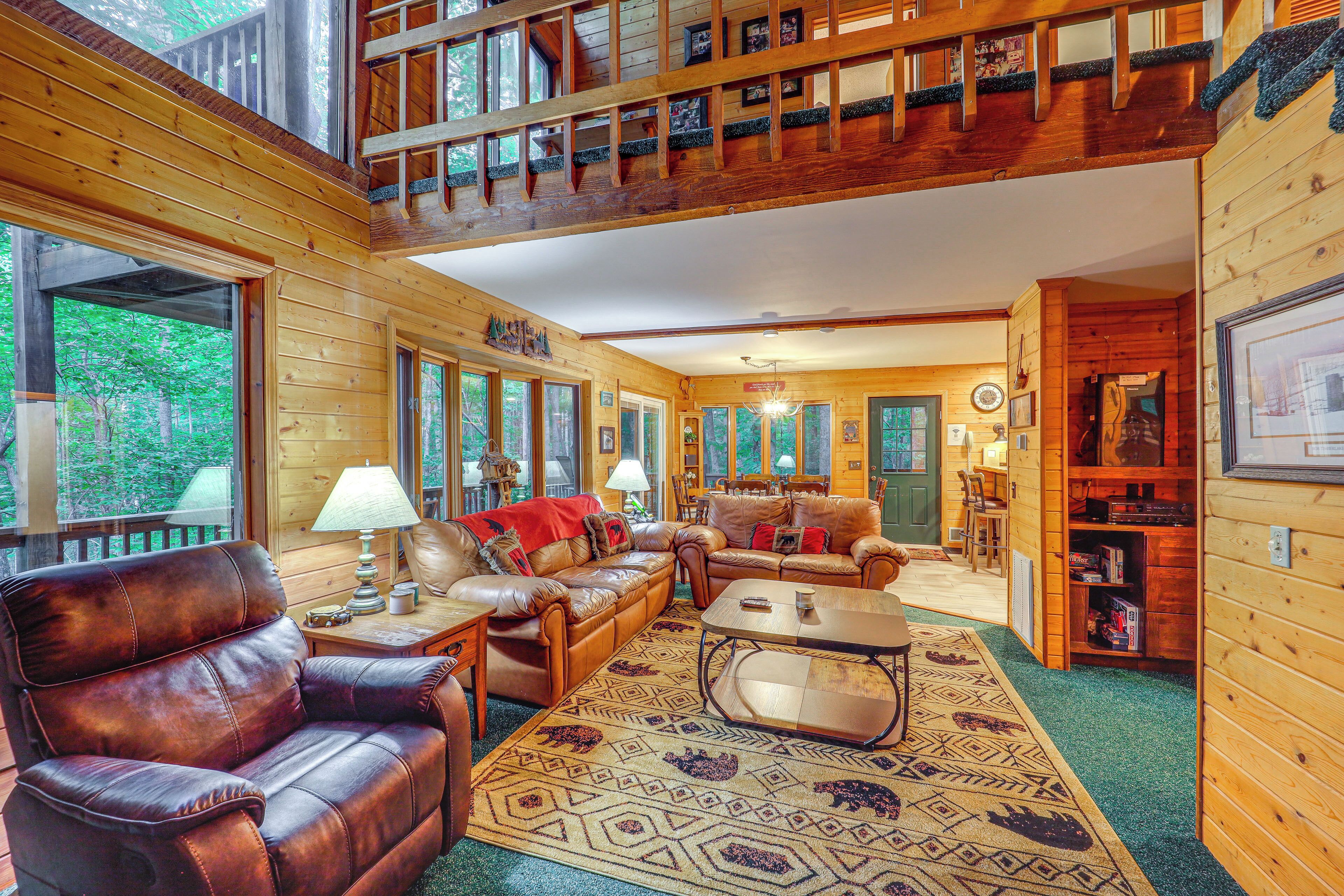 A cozy log cabin interior with a living room featuring leather sofas, a coffee table, and a patterned rug.