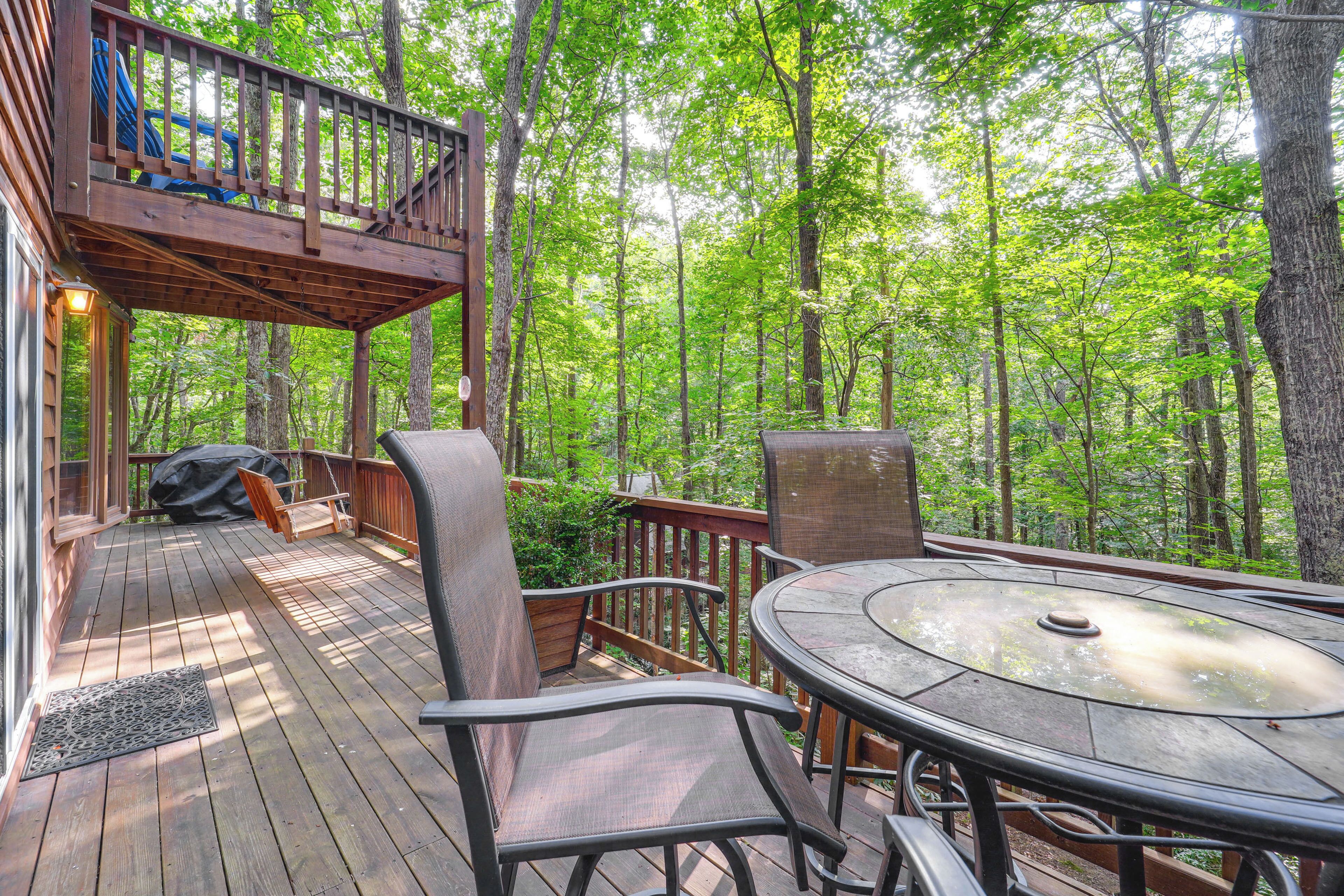 A wooden deck with a table and chairs, surrounded by a forest.