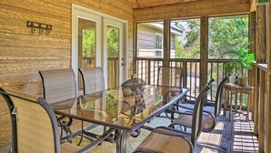 A wooden deck with a glass table and chairs, a wicker basket, and a small table with a plant. - Screened Deck: Cozy Branson West Cabin! (Branson West)