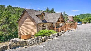 A two-story wooden cabin with a stone foundation, a wooden porch, and a car parked in the driveway. - Screened Deck: Cozy Branson West Cabin! (Branson West)