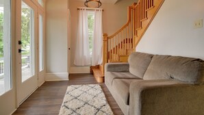 A modern living room with a wooden staircase, a beige sofa, and a patterned rug. - Waterfront Home w/ Hot Tub in Wrightsville! (Wrightsville)