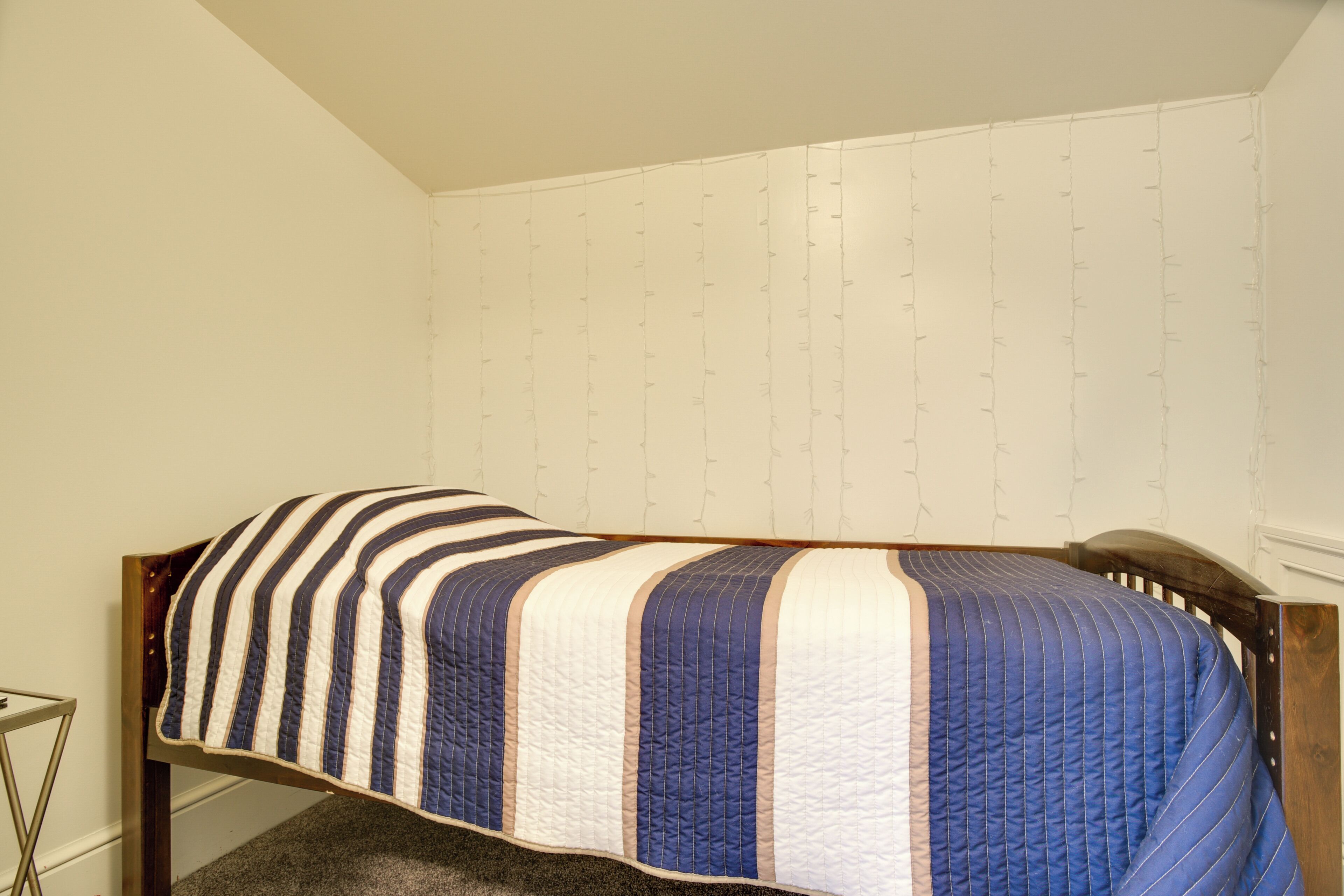Un lit simple avec une couette à rayures, dans une pièce aux murs unis et dotée d’une tête de lit en bois.