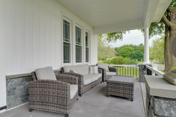 A covered porch with wicker furniture and a stone table. - Waterfront Home w/ Hot Tub in Wrightsville! (Wrightsville)