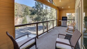 A wooden deck with wicker chairs, a grill, and a view of trees and a road.