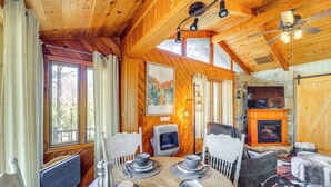 Un acogedor interior de cabaña con detalles de madera, una chimenea y un comedor con mesa dispuesta para cuatro.
