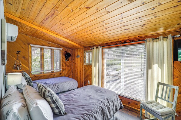 A wooden cabin room with two beds, a chair, and large windows. - Near Lake + Trails: Rustic Newland Cabin w/ Deck! (Newland)