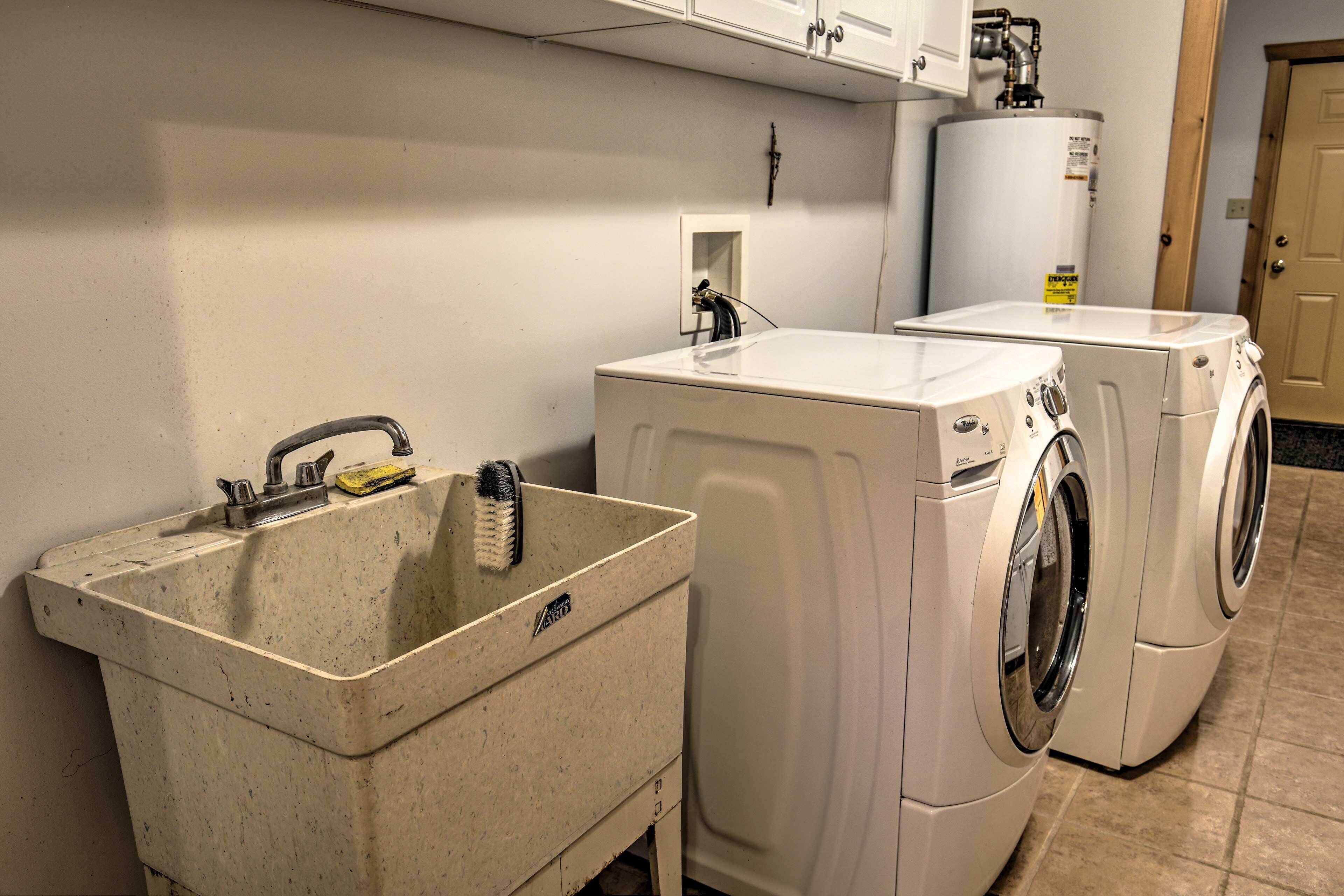 Un espace buanderie comprenant un évier, deux machines à laver et un chauffe-eau.