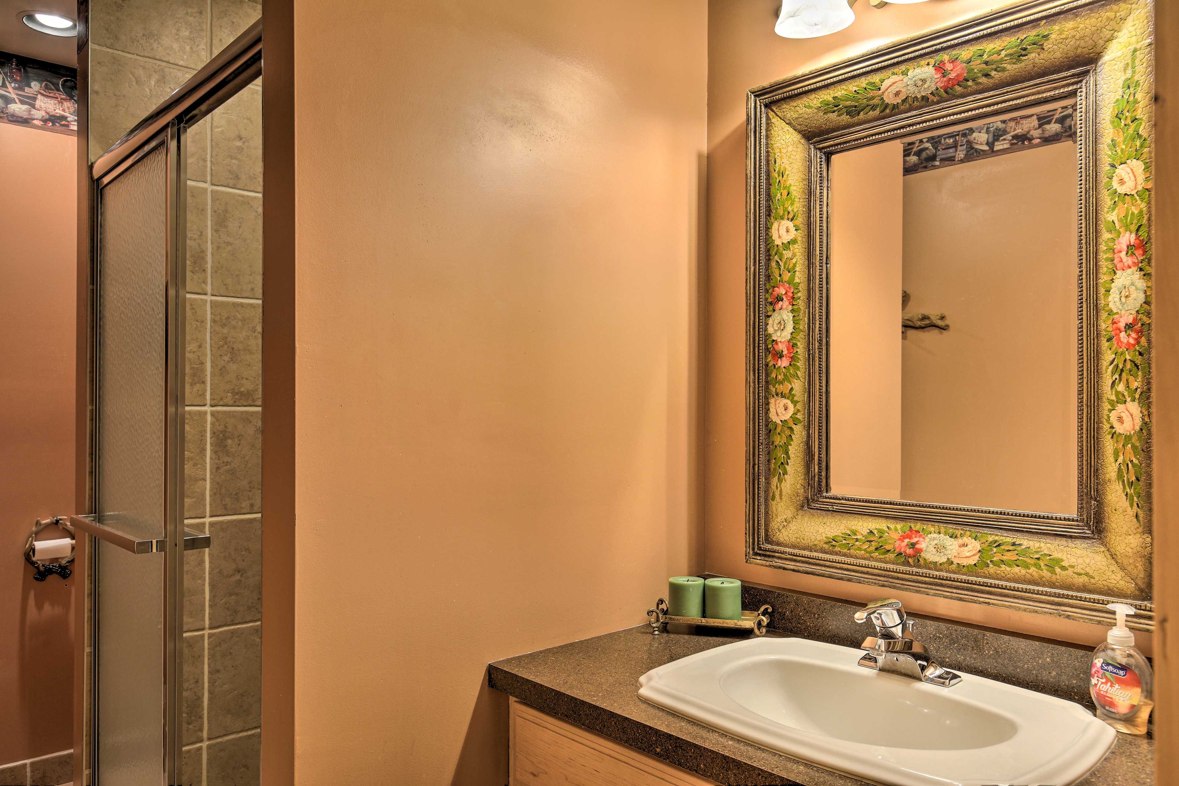 A bathroom with a shower, a sink, and a mirror with floral designs.