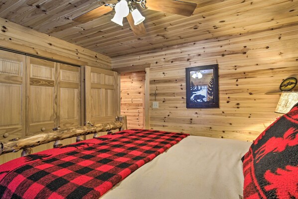 A wooden cabin room with a bed, a wooden bench, and a ceiling fan. - Waterfront Pike Lake Retreat: Snowmobile Paradise (Park Falls)