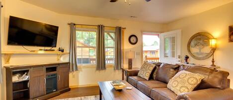 A living room with a flat-screen TV, leather sofa, wooden coffee table, and a ceiling fan.