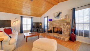 Amplia sala de estar con chimenea de piedra, techo de madera y un espacio de descanso acogedor.