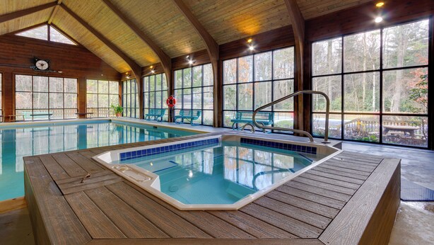 Piscina interior con mobiliario de cubierta de madera y amplias ventanas que ofrecen vistas del bosque circundante.