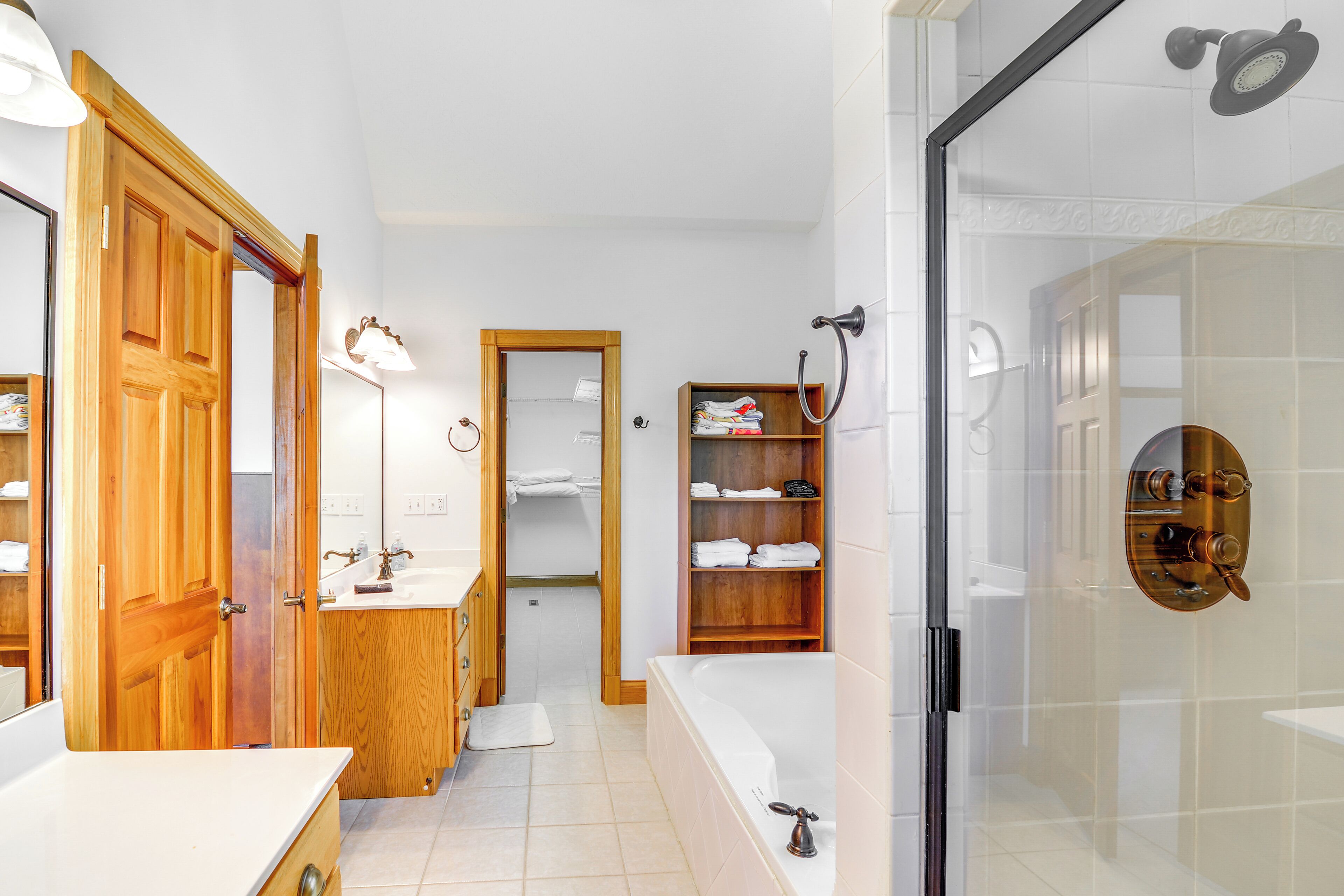 A bathroom with a wooden vanity, a glass shower enclosure, and a built-in shelf with towels.