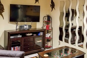 A living room with a flat-screen TV, a wooden entertainment unit, a glass coffee table, and a decorative mirror. - 1 Block to Shore: Family Condo in Myrtle Beach! (Myrtle Beach)