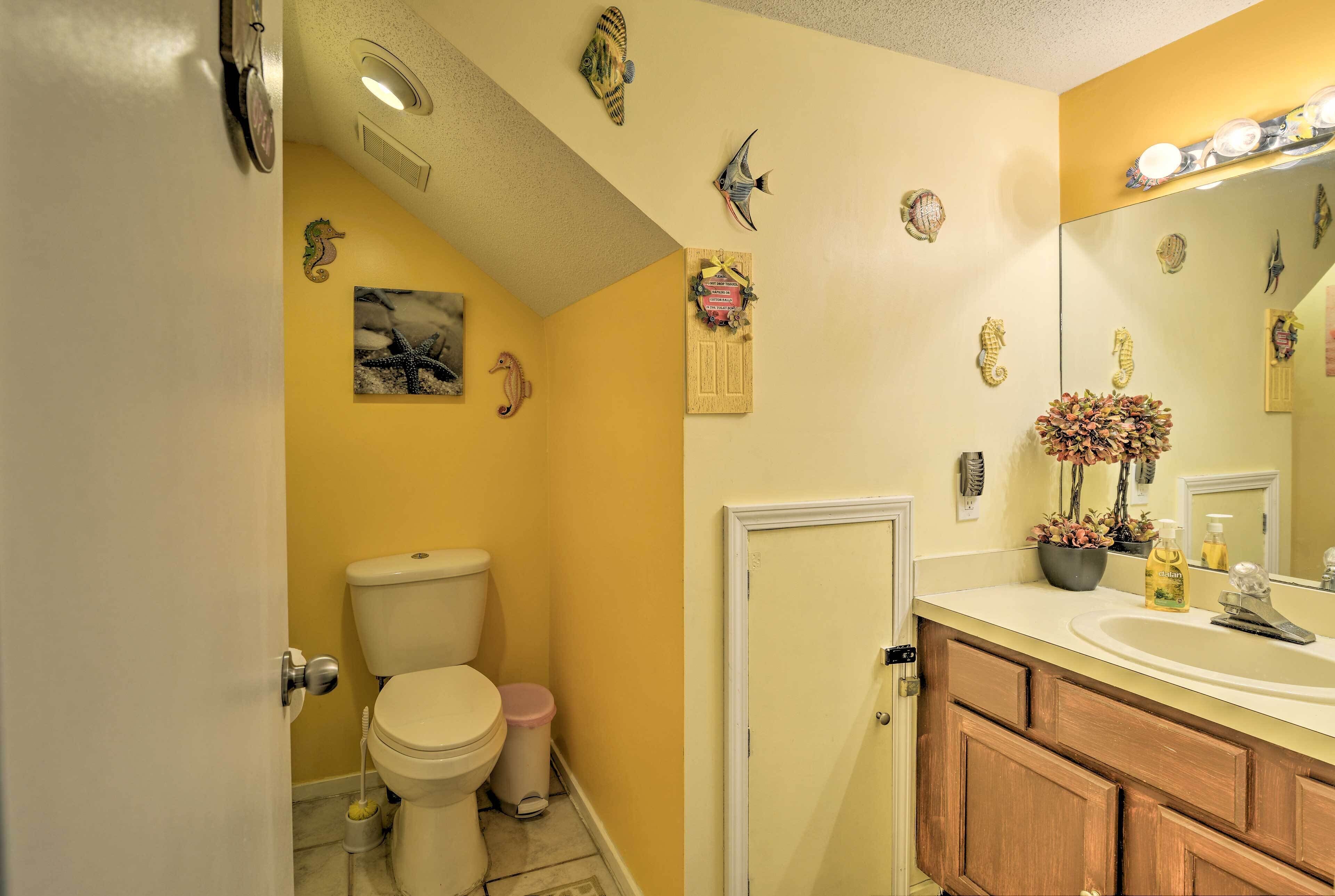 A bathroom with a toilet, sink, mirror, and decorative fish and seahorse wall art.