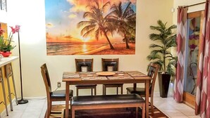 A dining area with a wooden table, four chairs, and a bench. There is a painting of a sunset and palm trees on the wall. - 1 Block to Shore: Family Condo in Myrtle Beach! (Myrtle Beach)