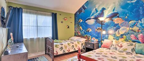 A bedroom with two beds, a desk, and a mural of an underwater scene.