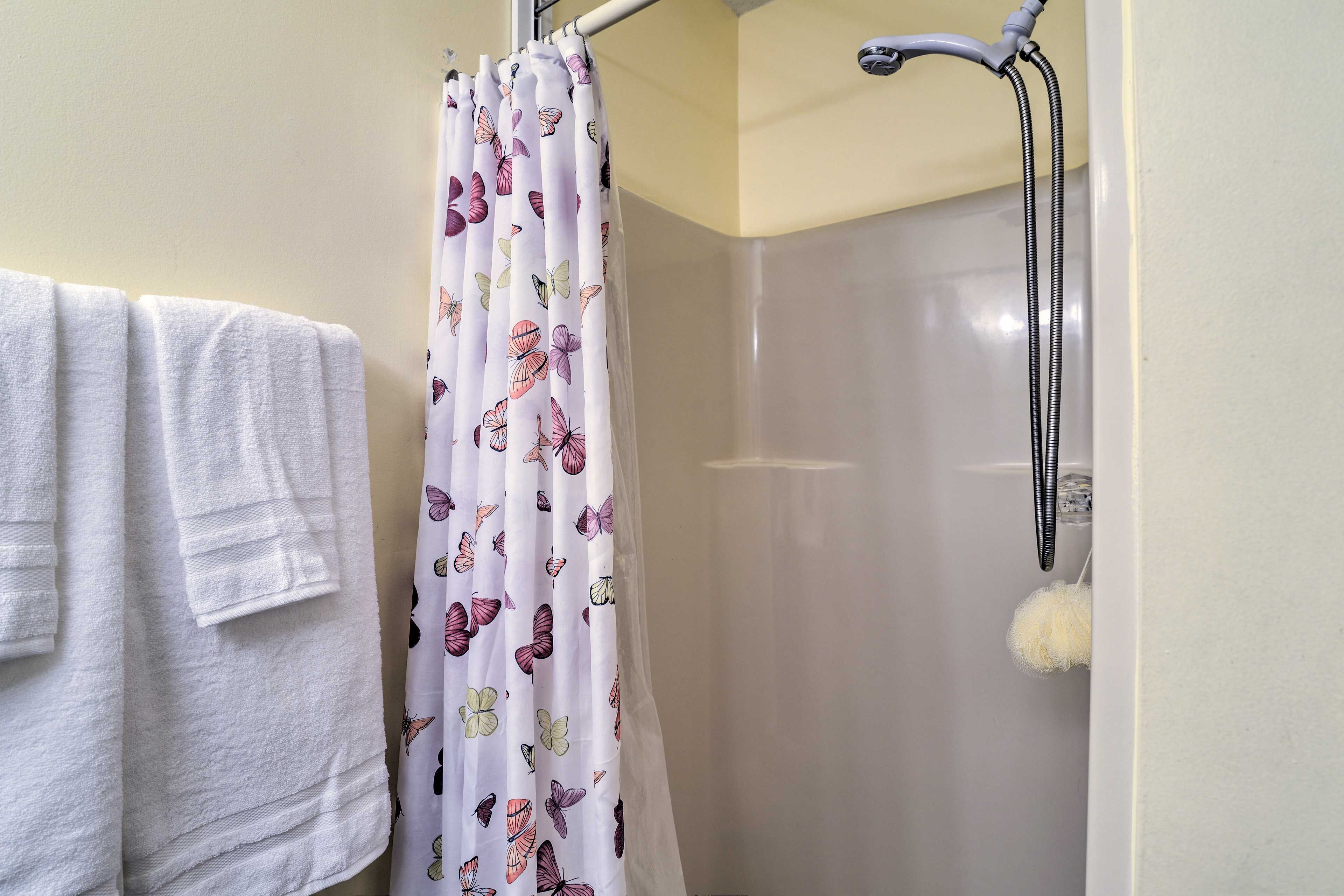 A bathroom with a shower curtain featuring a butterfly pattern, a white towel hanging on a rack, and a handheld showerhead.