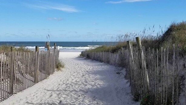 A sandy beach path leading to the ocean, flanked by wooden fences and vegetation. - 1 Block to Shore: Family Condo in Myrtle Beach! (Myrtle Beach)