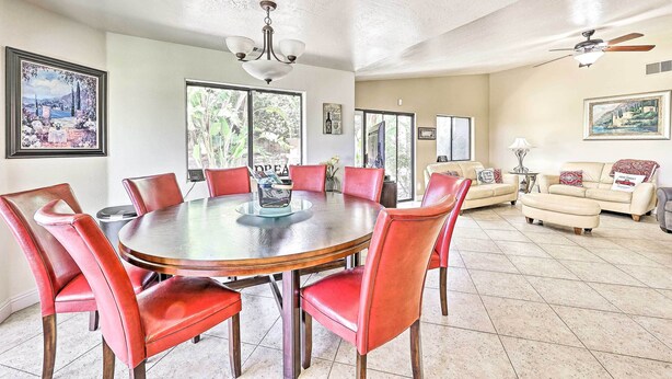 A dining area with a round table and red chairs, a ceiling fan, and a sofa in a living room with a view through large windows. - Spacious & Private Wine Country Villa w/ View (Temecula)