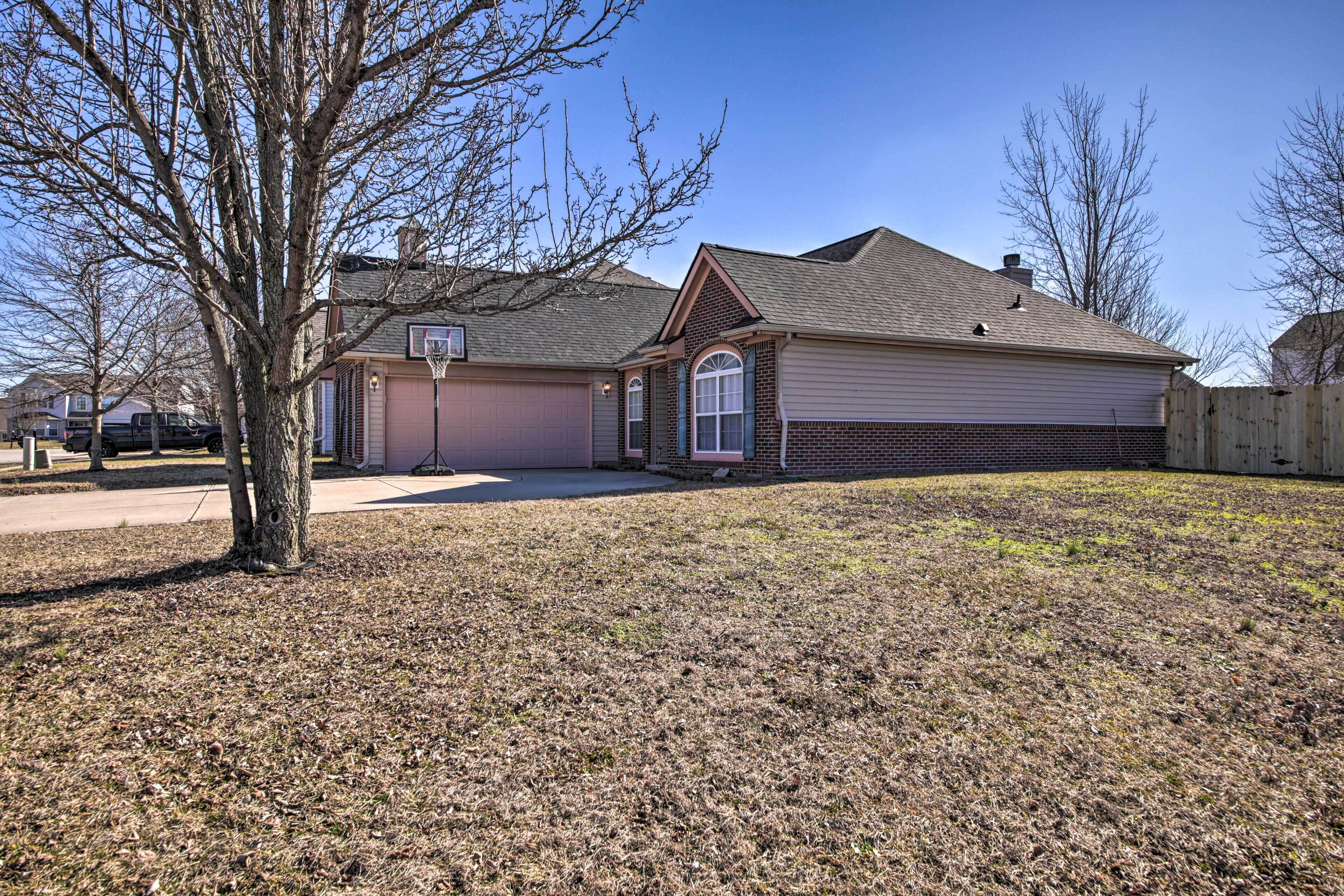 A single-story house with a front yard, a basketball hoop, and a wooden fence.