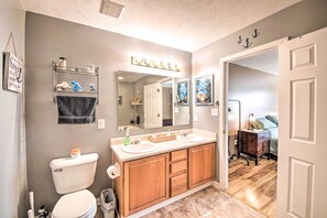 Features a dual sink vanity with a large mirror, wooden cabinet storage, and a wall-mounted towel rack.