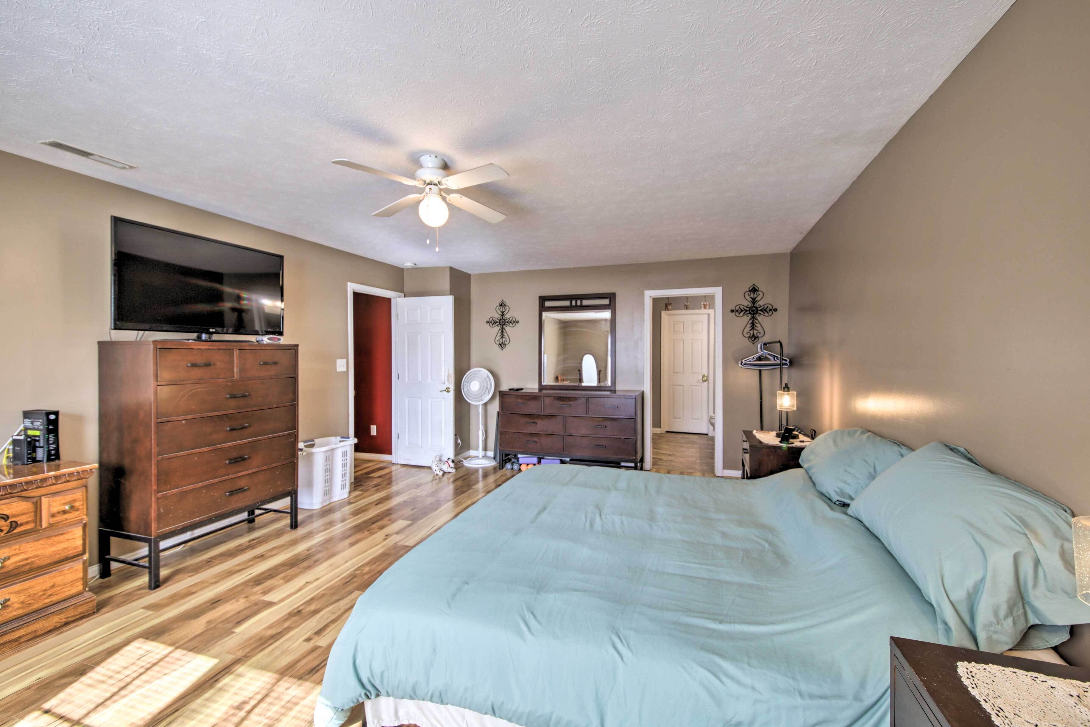 Une chambre à coucher comprenant un lit, une commode, un téléviseur, un ventilateur de plafond et un miroir.