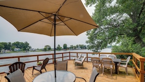 Um terraço com mesa e cadeiras, um guarda-sol grande e vista para um rio.