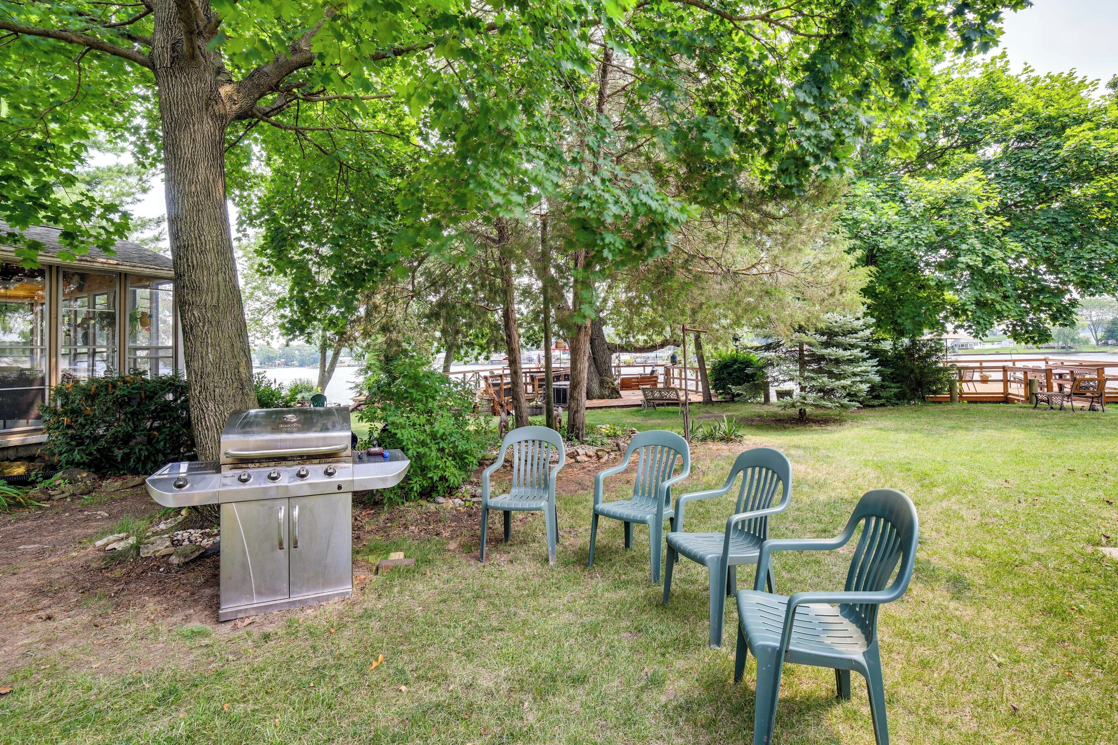 A backyard with a grill, chairs, and a view of a lake.