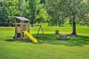 A wooden play structure with a slide and swings in a grassy park area.