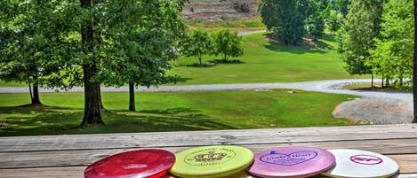 Un banco de madera con cuatro frisbees, con vista a un área verde con árboles y una carretera.