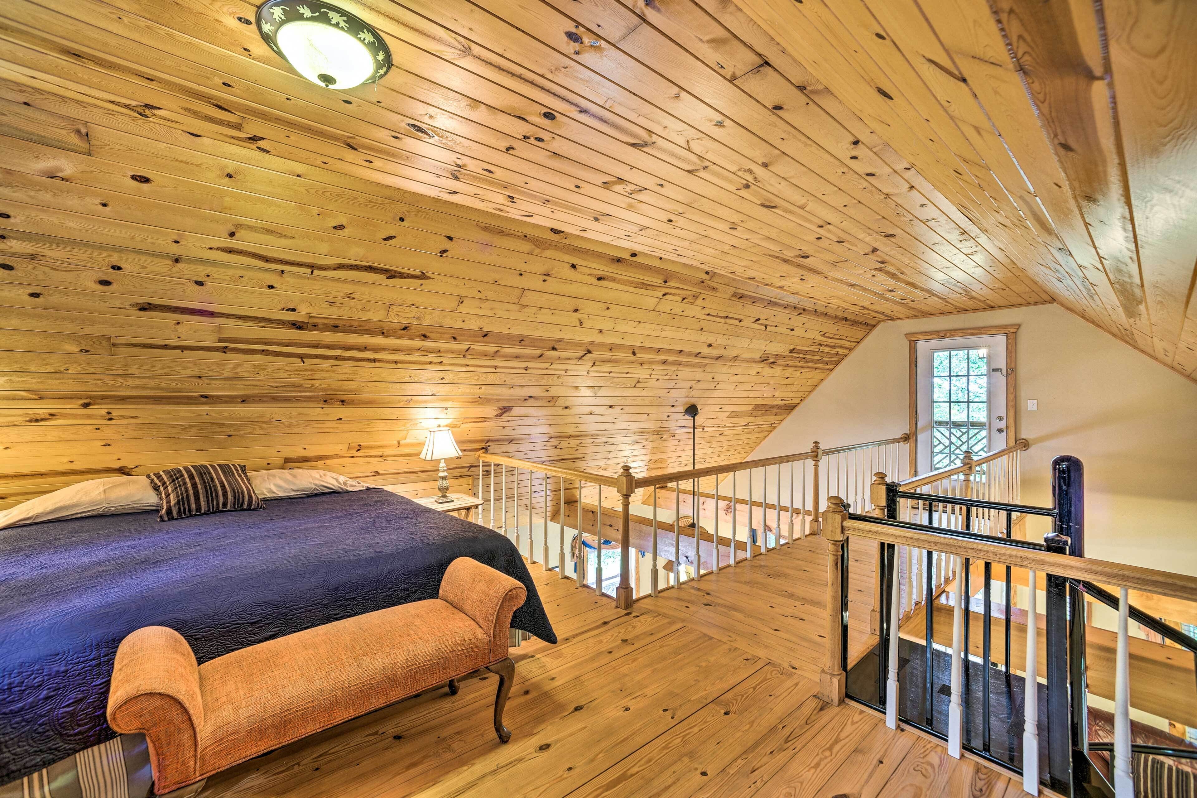 Een slaapkamer met een houten plafond, een bed met een blauwe deken, een houten bankje en een trap naar een hoger gelegen niveau.