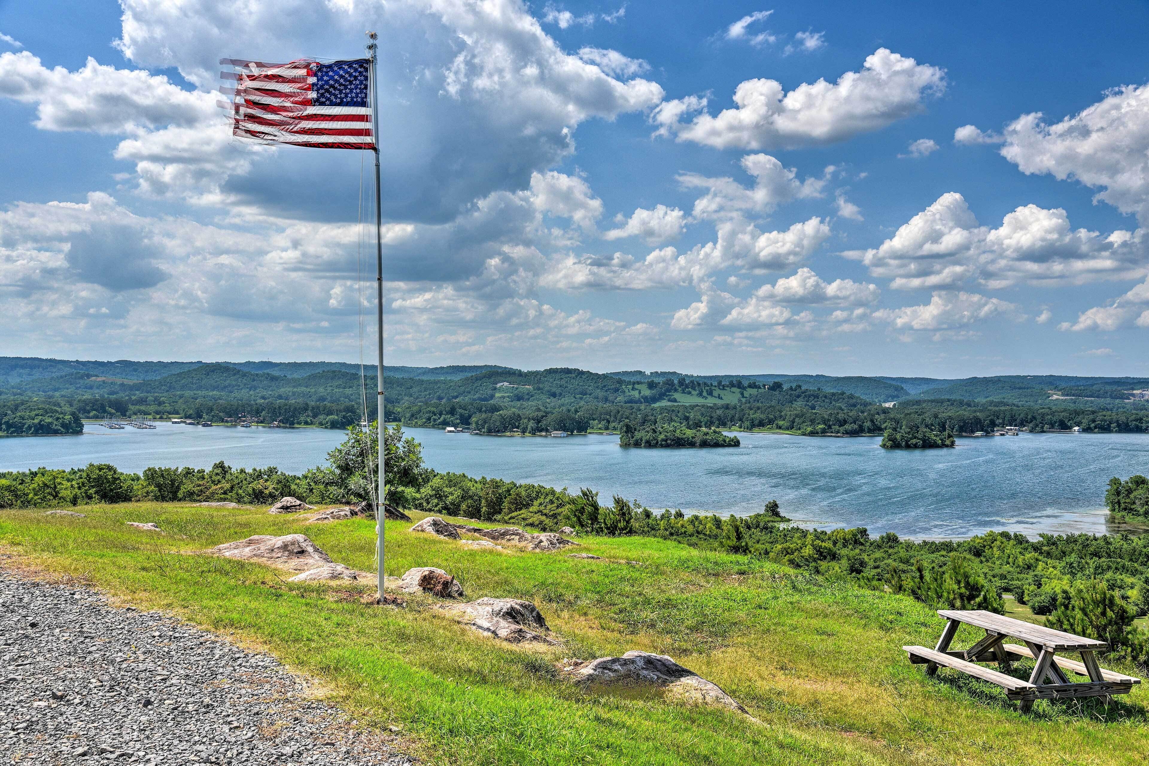 A flagpole with an American flag, a picnic table, and a lake with islands in the background.