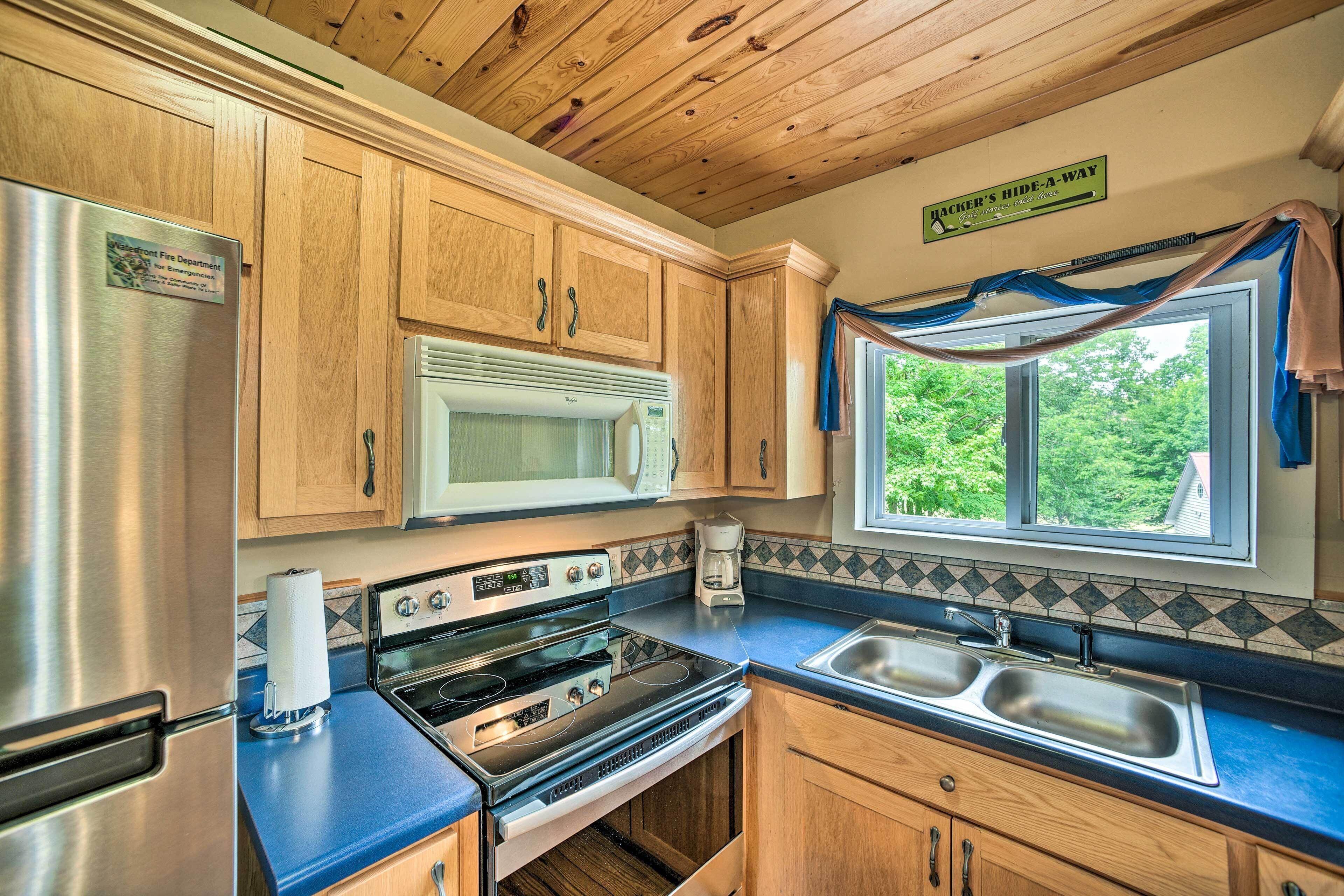 A kitchen with wooden cabinets, stainless steel appliances, a microwave, and a window with a view of greenery.