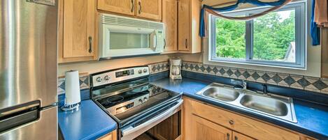 A kitchen with wooden cabinets, stainless steel appliances, a microwave, and a window with a view of greenery.