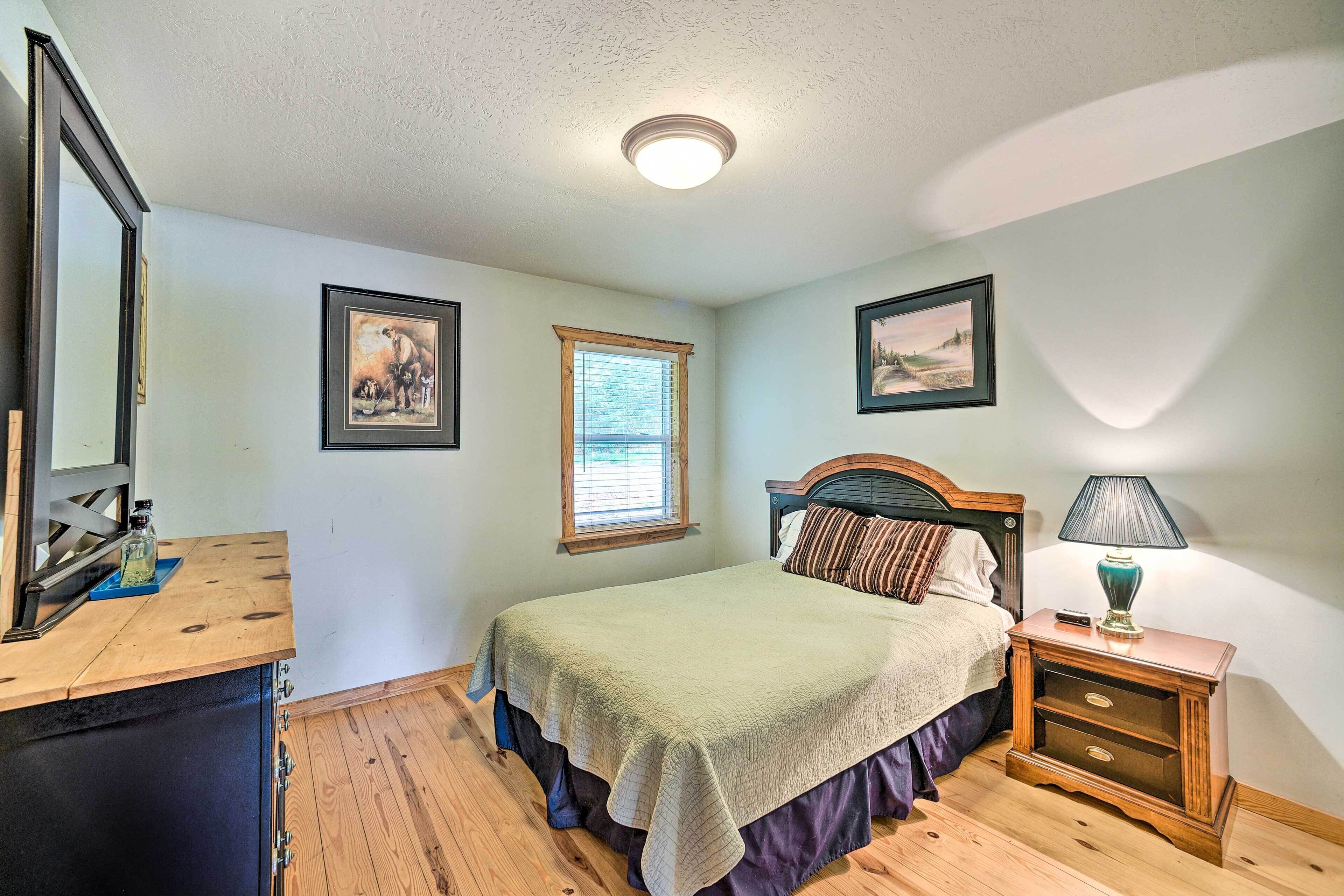 A bedroom with a bed, a nightstand with a lamp, a window, and framed pictures on the wall.