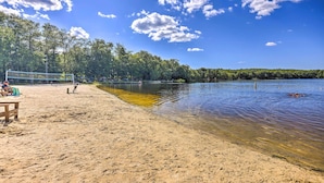 Ein Strand mit Volleyballnetz, klarem Wasser und Bäumen im Hintergrund.