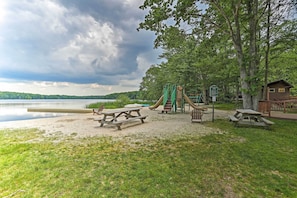 A lakeside park with picnic tables, a playground, and a cabin.