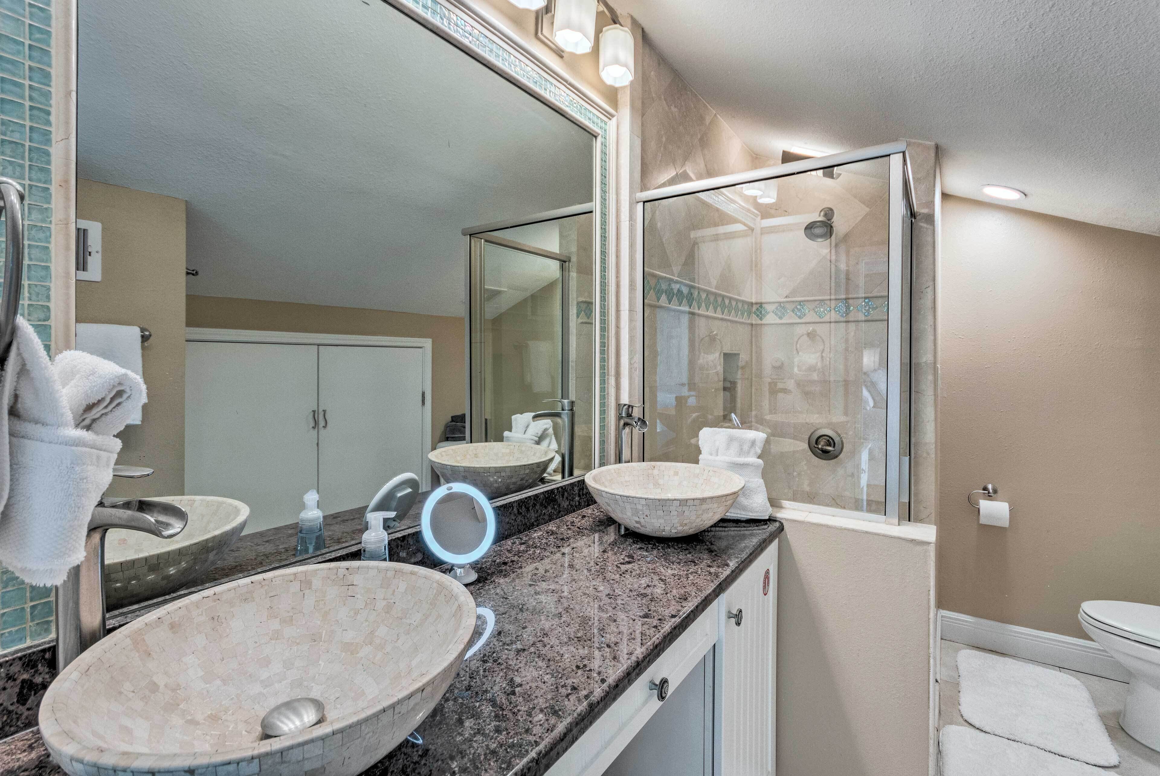 A bathroom with a large mirror, two sinks, a shower, and a toilet.