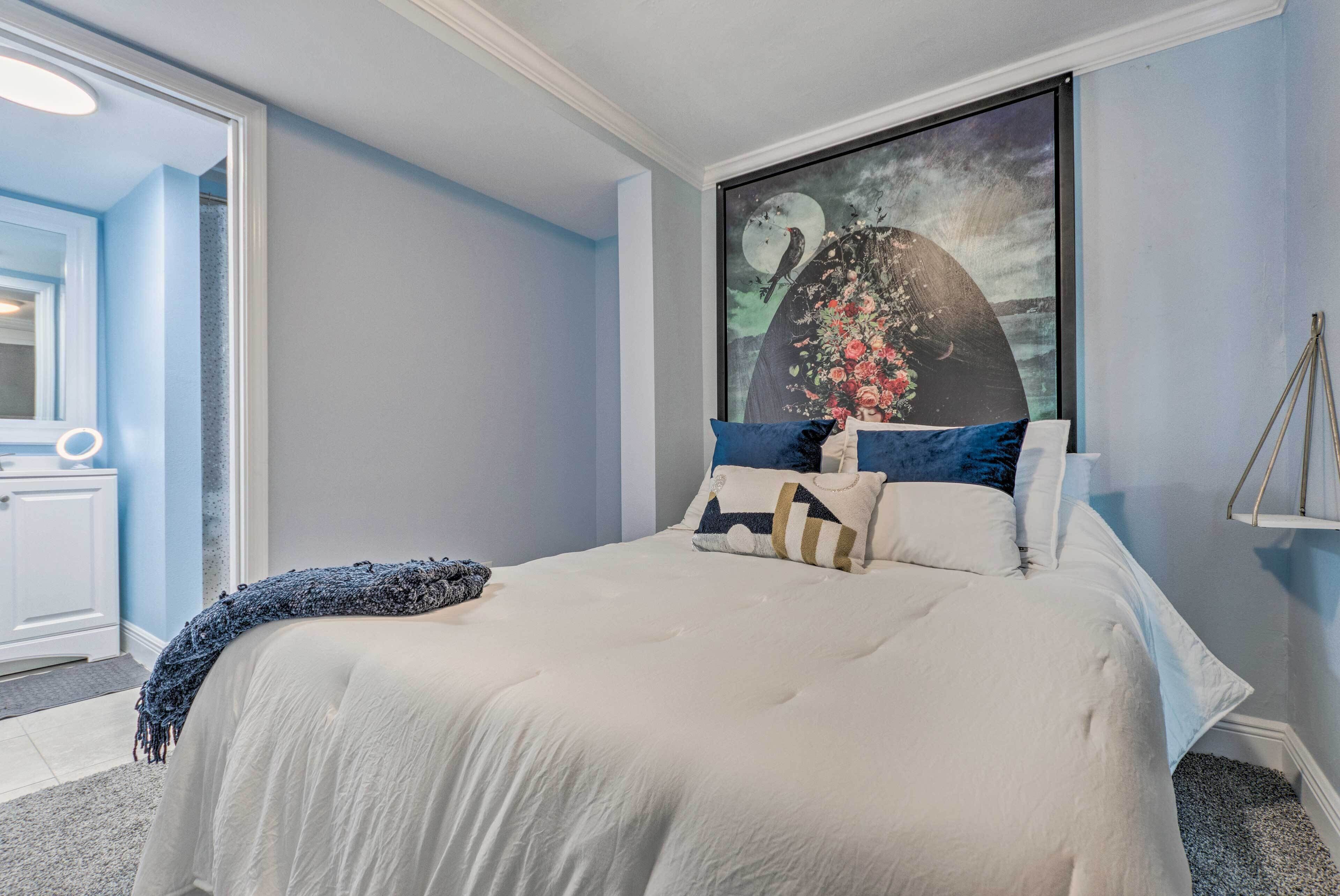 A bedroom with a large bed, a painting of a bird and flowers on the wall, and a bedside table with a lamp.