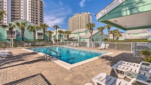 A swimming pool with lounge chairs, palm trees, and tall buildings in the background. - Vibrant Family Condo: 100 Feet to Private Beach! (Miramar Beach)