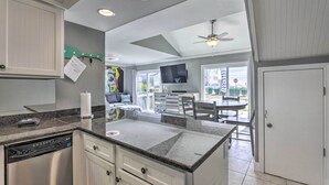 A kitchen with a dishwasher, white cabinets, a granite countertop, and a dining area with a table and chairs. - Vibrant Family Condo: 100 Feet to Private Beach! (Miramar Beach)