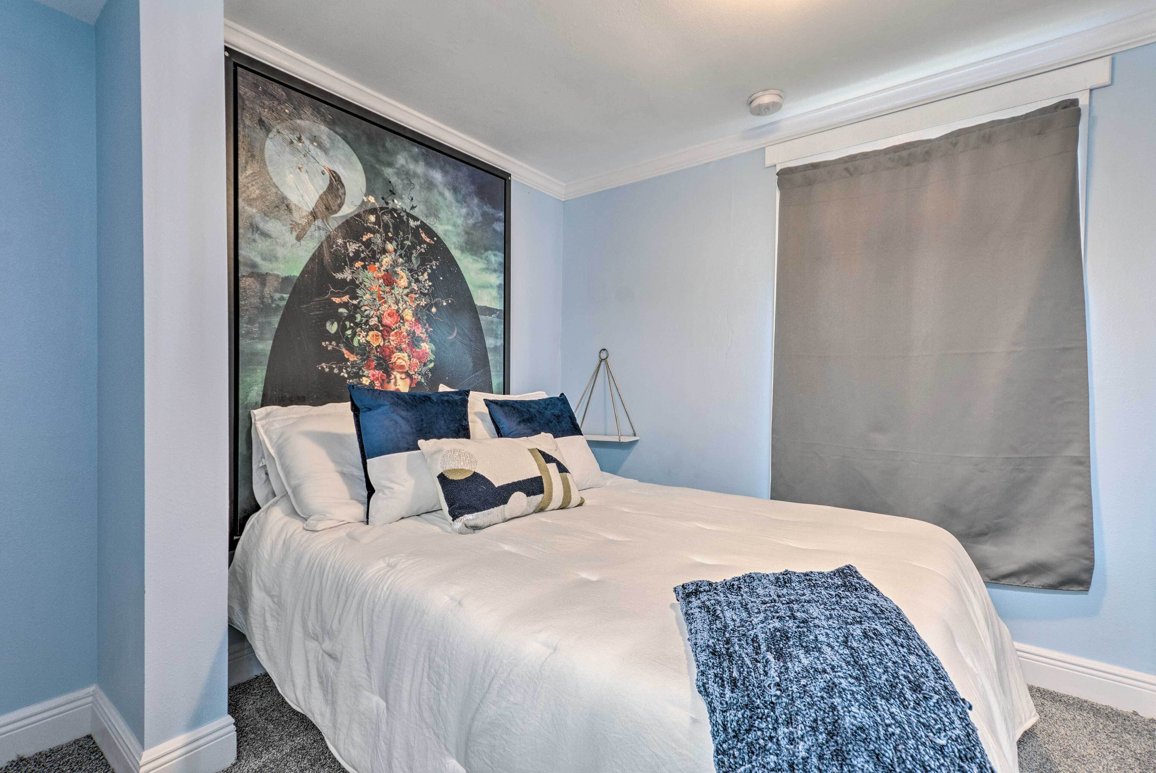 Un dormitorio con una cama, un cuadro grande y una ventana con cortina.