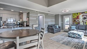 A modern kitchen with built-in appliances, a dining area with a round table and chairs, and a living room with a sofa and ottoman. - Vibrant Family Condo: 100 Feet to Private Beach! (Miramar Beach)