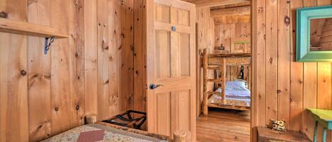A wooden cabin room with a bed, a door leading to another room, and a small table with a lamp.